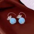 Close-up of blue textured round bead earrings with silver flower-shaped hooks on fabric. - Hook Style / Silver-Blue