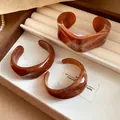 Close-up of irregular marbled acrylic bangles in amber tones displayed in a jewelry tray - Brown