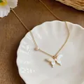 Macro view of dainty gold necklace with iridescent butterfly and pearl detail on a white shell. - Gold-White