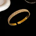 Primer plano de un elegante brazalete abierto dorado con tres filas de cristales brillantes. - Estilo de Tres Capas / Dorado