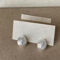 Macro view of silver teardrop stud earrings with zircon star pattern on textured cardstock - Silver