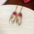 Primo piano di orecchini in resina con fiori secchi rosa e bianchi in ganci dorati. - Oro-Bianco-Rosa