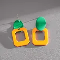 Primo piano di orecchini geometrici verdi e arancioni con aghi in argento su pelle. - Verde/Arancione-Giallo Contrasto