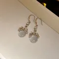 Detailed view of silver-tone hook earrings with shimmering rhinestones and round resin pendants. - Silver