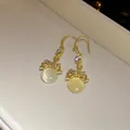 Detailed view of elegant gold ear hooks with circular resin pendants and small crystals. - Gold