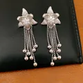 Detail of silver flower tassel earrings with sparkling cubic zirconia on black leather. - Flower Tassel Style / Silver