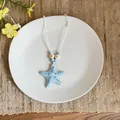 Blue ceramic starfish necklace with white cord on a minimalist plate. - Blue