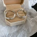 Détail de boucles d'oreilles créoles vagues argentées dans un écrin en velours beige. - Boucles d'Oreilles Ondulées Irrégulières à Trois Couches / Argent