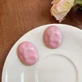 Detail shot of pink macaron oval acrylic earrings with gold edge on white saucer. - Pink