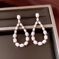 Close-up of elegant vintage teardrop earrings with white stone inlay on jewelry display tray. - White
