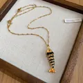 Detailed view of a fashionable gold-tone fish pendant necklace in a wooden display tray - Fish Pendant (Gold Chain) / Black
