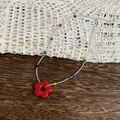 Macro detail of the vibrant red flower pendant and colorful beads on a silver necklace chain - Necklace / Red