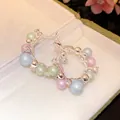 Close-up detail of silver hoop earrings featuring colorful pastel pearls and clear zircons. - Gold