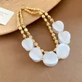 Close-up detail of a luxury double-layer necklace with gold beads and white acrylic disks. - Necklace / White