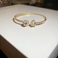 Close-up detail of golden heart-shaped zircon open cuff bracelet with sparkling gemstones - Cuff Bracelet / Gold