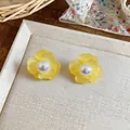 Close-up of fresh yellow flower stud earrings with elegant pearl center on a tray - Yellow