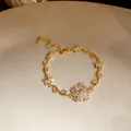 Vue macro d'un bracelet plaqué or 18 carats avec détails de fleurs et feuilles en zircon. - Or-Blanc