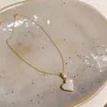 Nahaufnahme einer funkelnden Herz-Halskette mit Zirkonia auf einem Keramikteller - Halskette / Gold
