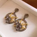 Close-up of vintage floral drop earrings with gold leaves and gunmetal crystal flowers - Gold And Gunmetal Black