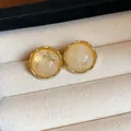 Close-up of vintage resin stud earrings with gold-tone borders and ivory marble texture - Textured Round / Gold