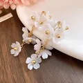Close-up of white acrylic flower tassel earrings with elegant gold chain details. - White
