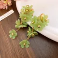 Detailed macro view of green acrylic flower tassel earrings with golden bead centers - Green