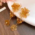Close-up of amber acrylic flower tassel earrings with golden chains on white plate - Brown