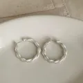 Primer plano detallado de aretes de aro plateados con textura esmerilada girada - Estilo de Pasador de Plata / Plateado