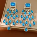Detailed close-up of blue crystal teardrop tassel earrings on a luxury jewelry box. - Square Teardrop Tassel Style / Blue