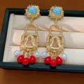 Detailed view of ornate gold lock earrings with pearls and red tassels in a box. - Silver Earring Post Style / Gold-Blue-Red