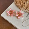 Dettaglio di orecchini a lobo a forma di fiore rosa con bordo dorato su un libro - Rosa