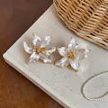 Primo piano di orecchini a lobo a fiore bianco perlato con bordi dorati su un libro - Beige