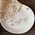 Dettaglio di collana multistrato con pietre rosa e perle bianche su un piatto crema - Bianco + Rosa