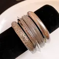 Dettaglio di quattro bracciali rigidi in metallo argento con diverse texture su supporto nero. - Set da 4 pezzi / Argento