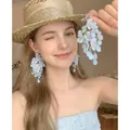 Detailed view of blue fabric flower tassel earrings worn by a model in a summer hat. - Blue
