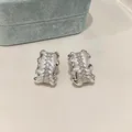 Detailed macro shot of silver pleated C-shaped earrings featuring rows of square zircons - Pleated C-Shape Style / Silver White