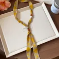 Close-up detail showing a chiffon printed scarf necklace with decorative wooden beads. - Yellow