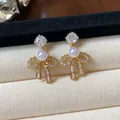 Close-up of elegant 18k gold plated bow earrings with pearls and sparkling zircons. - Bowknot Stud Earrings / Gold