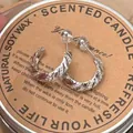 Elegant silver twisted hoop earrings with sparkling zircon stones on a rustic candle lid - Silver
