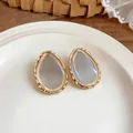 Detailed view of teardrop resin stud earrings with a gold wavy textured metal frame - Gold Frame / 925 Silver Needle / White