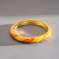 Detail view of a gold-toned bangle featuring vibrant yellow and orange enamel patterns. - Gold Yellow Orange Enamel Metal Bangle