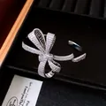 Macro view of a luxury 18K gold plated zircon encrusted bow open bangle in a black box - Silver
