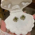 Dettaglio di orecchini a lobo con zircone verde oliva in una scatola a conchiglia - Orecchino Halo Rotondo / Argento-Verde