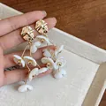 Close-up of gold tassel earrings with white acrylic flowers and metallic studs. - White