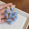 Close-up of light blue acrylic flower tassel earrings with gold-toned metal accents. - Blue