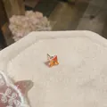 Primo piano di un orecchino a lobo in zircone quadrato su un supporto in lino. - Pezzo Singolo / Arancione