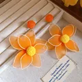 Macro detail of sweet orange mesh flower earrings with woven centers in a jewelry box - Silver Earring Post Style / Orange
