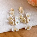 Elegant white acrylic flower tassel earrings with decorative golden metallic accents - Khaki