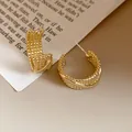 Detailed macro view of elegant gold C-shaped hoop earrings with a retro woven texture - Gold