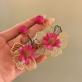Hand-held view of vibrant magenta raffia flower drop earrings with gold hollow petals. - Style 8 (Silver Pin-Gold) / Rose Red
